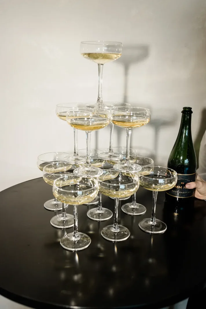 A tower of coupe glasses on a round table, bottle and hand
