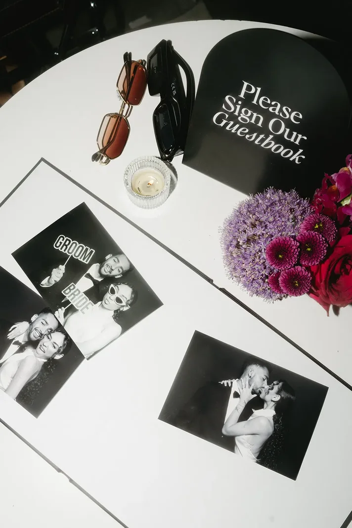 A guestbook on a white table with photo booth prints and flowers