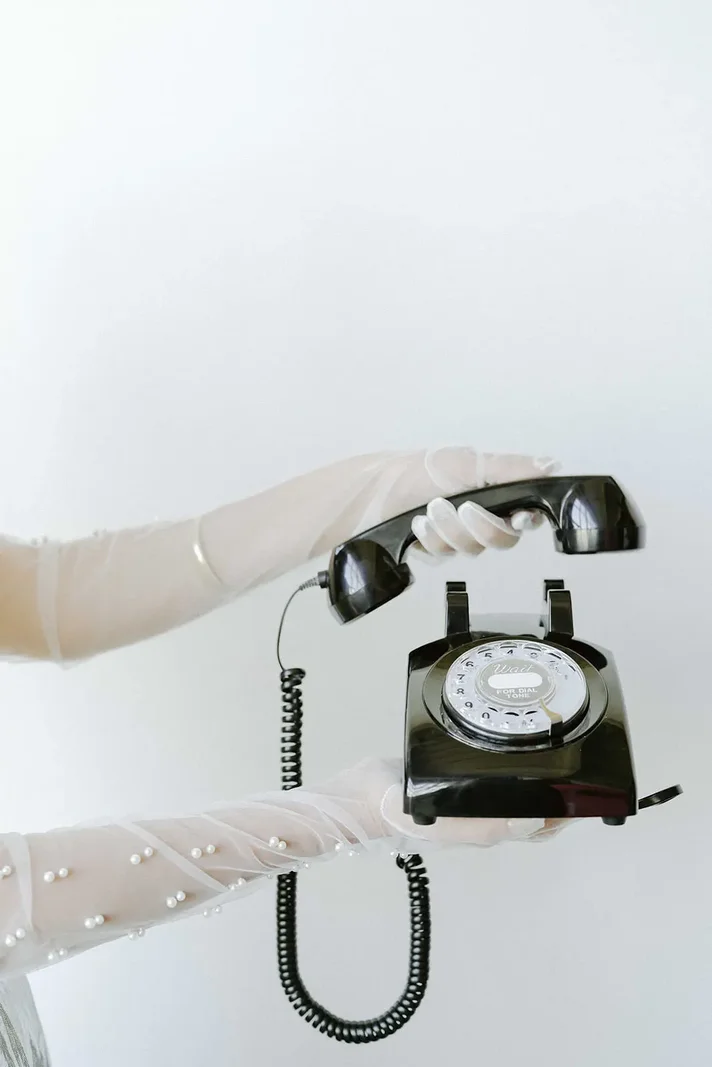 A pair of gloved hands holding a black rotary telephone
