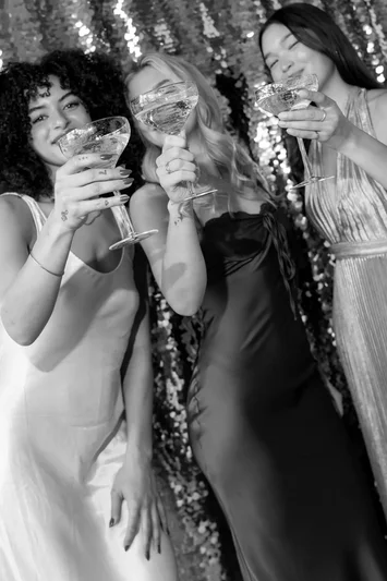 Guests in sequined dresses raising a toast in a black and white photo strip